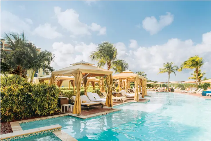 Elegant cabanas by the pool surrounded by lush greenery and palm trees.