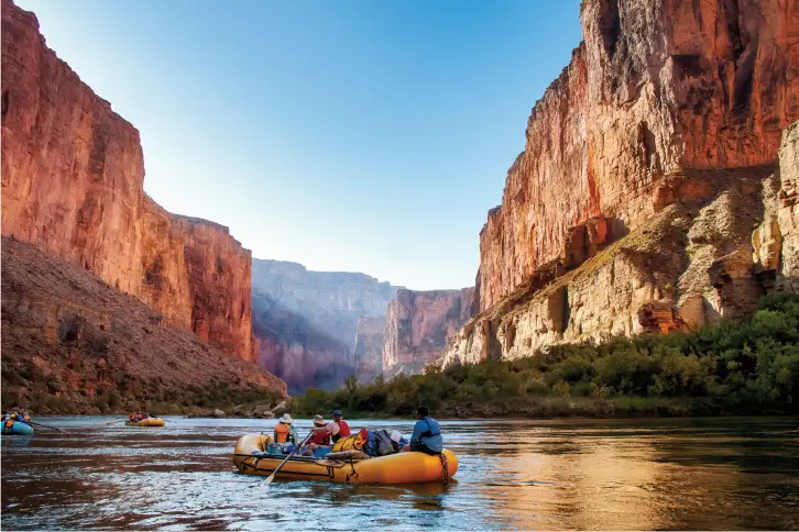 Explorers navigating the river in the Grand Canyon with towering cliffs in the background.